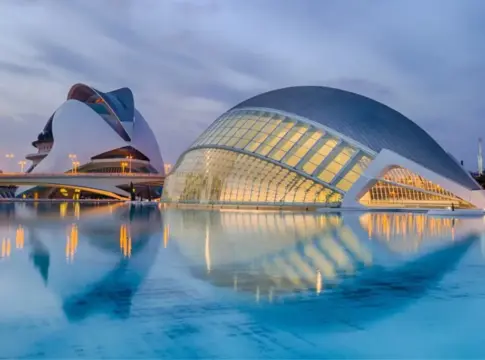 Edificios iluminados junto al agua Edificios modernos iluminados al anochecer se reflejan en una superficie de agua.