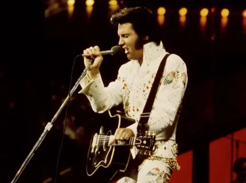 Elvis Presley cantando con guitarra Elvis Presley canta al micrófono mientras toca una guitarra en el escenario.