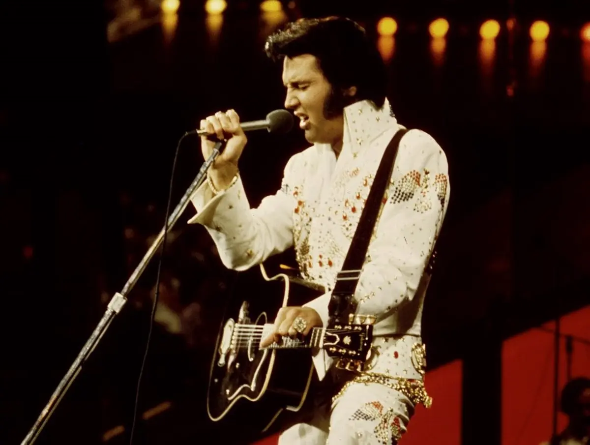 Elvis Presley cantando con guitarra Elvis Presley canta al micrófono mientras toca una guitarra en el escenario.