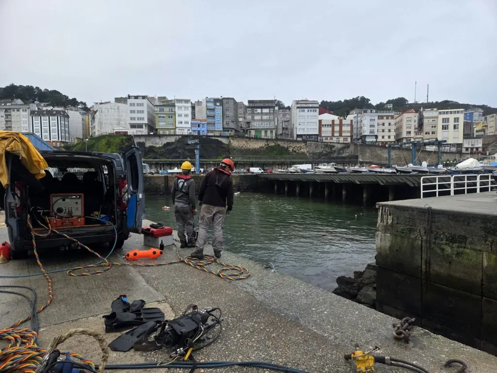 Dos personas junto a equipo de buceo en el muelle de un puerto