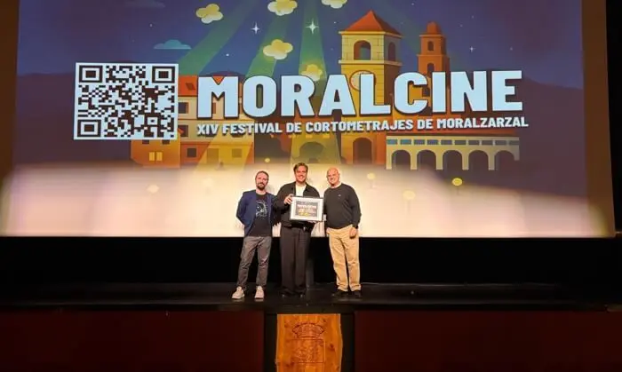 Tres hombres en el escenario de MoralCine Tres hombres posan en un escenario bajo una pantalla del festival MoralCine.