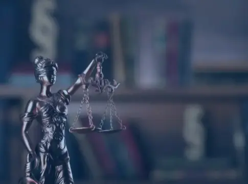 Estatua de la justicia con balanza Estatua de la justicia con balanza frente a una estantería de libros desenfocada.