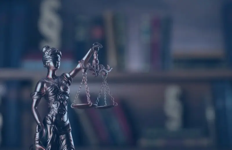Estatua de la justicia con balanza Estatua de la justicia con balanza frente a una estantería de libros desenfocada.