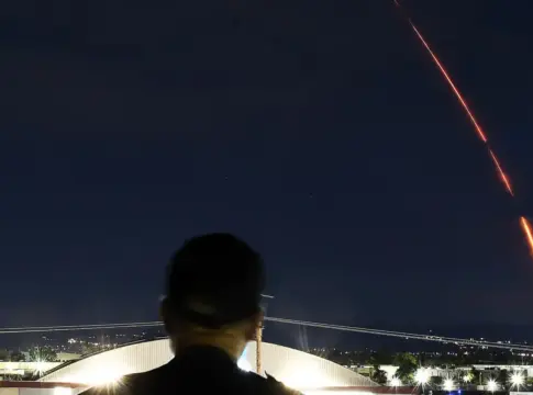 Estela luminosa en un cielo nocturno Una estela luminosa curva cruza el cielo nocturno sobre una persona en silueta.