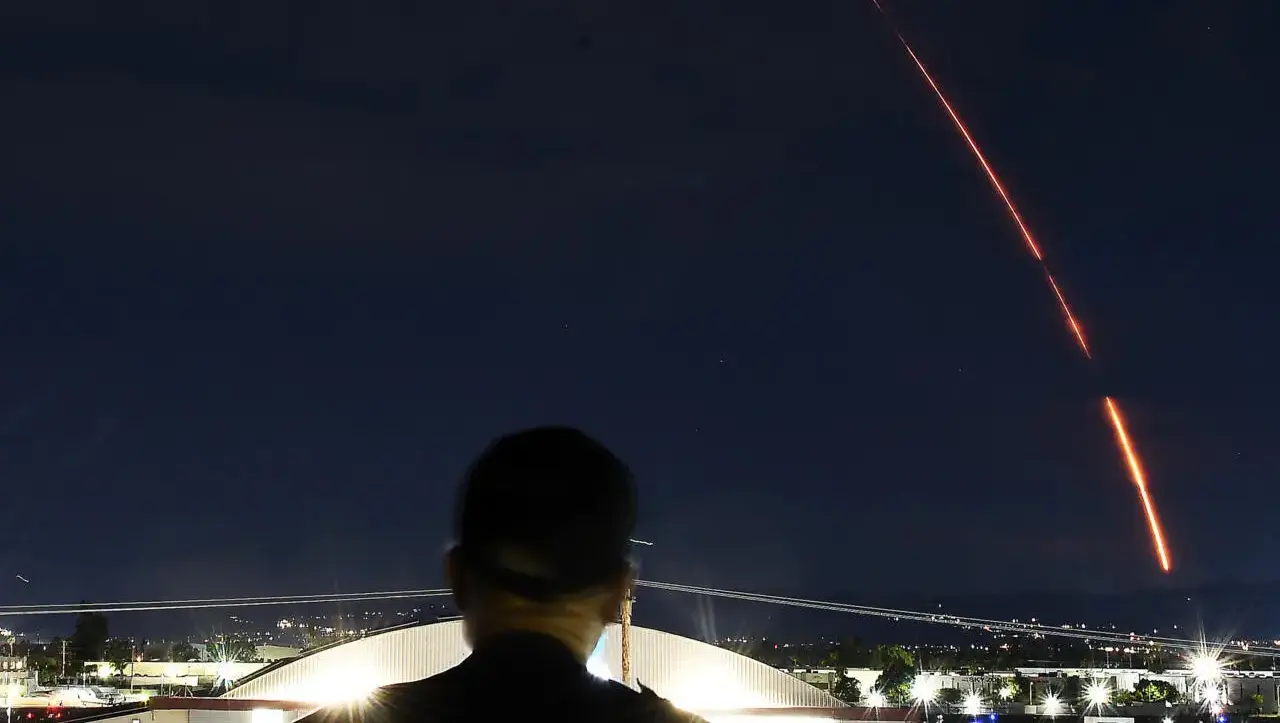 Estela luminosa en un cielo nocturno Una estela luminosa curva cruza el cielo nocturno sobre una persona en silueta.