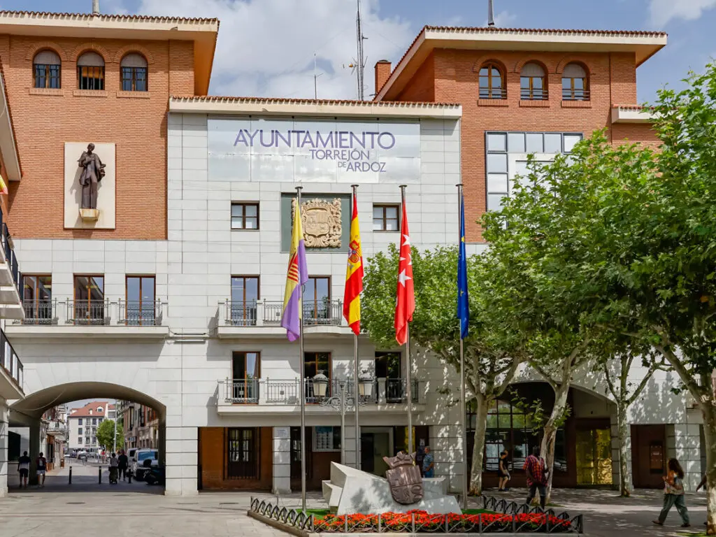 Fachada del Ayuntamiento de Torrejón de Ardoz con banderas y peatones en la plaza