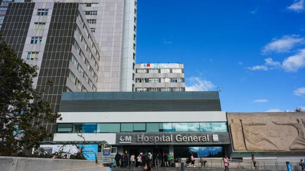 Exterior de un hospital con el rótulo Hospital General y personas junto a la entrada