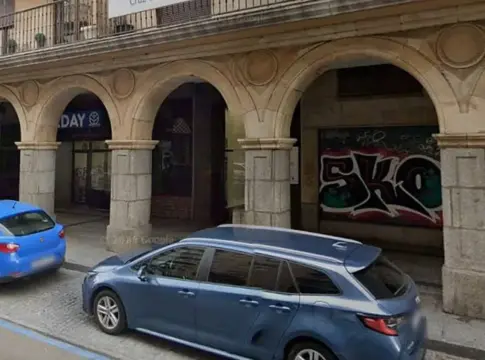 Fachada urbana con soportales y coches Fachada de piedra con soportales y varios coches estacionados junto a la acera.