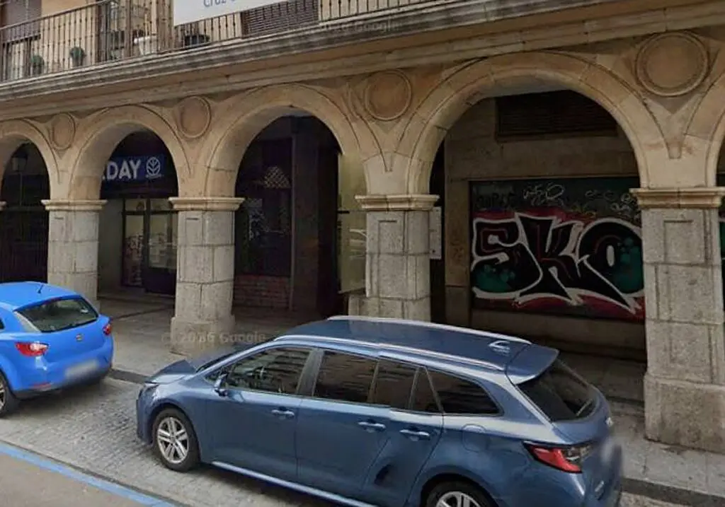 Fachada urbana con soportales y coches Fachada de piedra con soportales y varios coches estacionados junto a la acera.