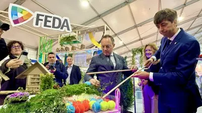 Personas visitan un estand de FEDA con plantas y elementos de colores sobre una mesa