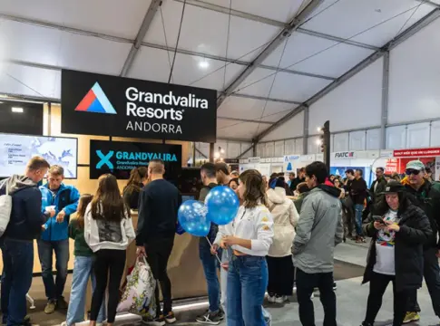 Estand de Grandvalira Resorts en la feria Estand de Grandvalira Resorts en una feria, rodeado de visitantes y globos azules.