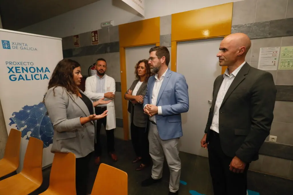 Grupo junto al cartel de Xenoma Galicia Varias personas conversan junto a un cartel del proyecto Xenoma Galicia en un hospital.
