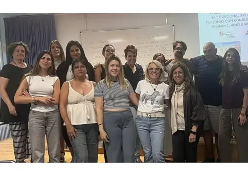 Grupo posa durante una jornada formativa Grupo de personas posa frente a una pizarra y una diapositiva de formación