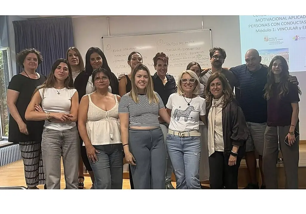 Grupo posa durante una jornada formativa Grupo de personas posa frente a una pizarra y una diapositiva de formación