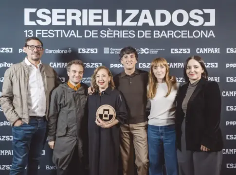 Grupo posa en el festival Serielizados Seis personas posan ante el cartel de Serielizados; una mujer sostiene un galardón.