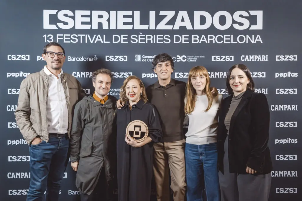 Seis personas posan ante el cartel de Serielizados; una mujer sostiene un galardón.