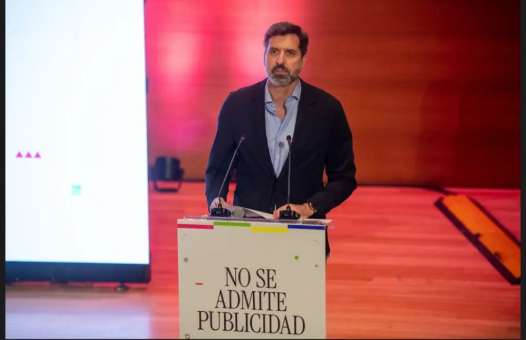 Hombre ante un atril con dos micrófonos en un escenario iluminado en rojo