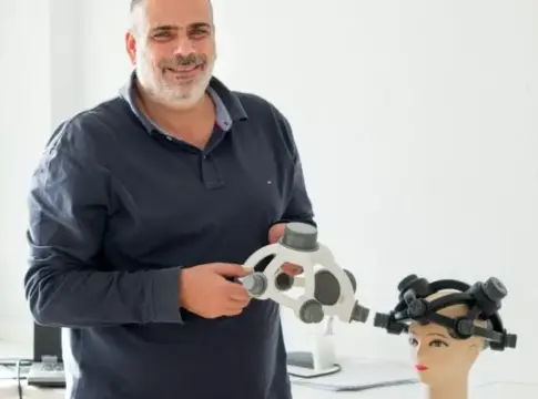 Hombre con dispositivo junto a maniquí Hombre sostiene un dispositivo junto a un maniquí con un sistema colocado en la cabeza.