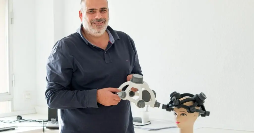 Hombre con dispositivo junto a maniquí Hombre sostiene un dispositivo junto a un maniquí con un sistema colocado en la cabeza.