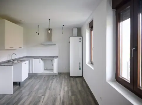 Interior de una cocina vacía Cocina vacía con muebles blancos, encimera gris, ventanas y suelo de aspecto madera.