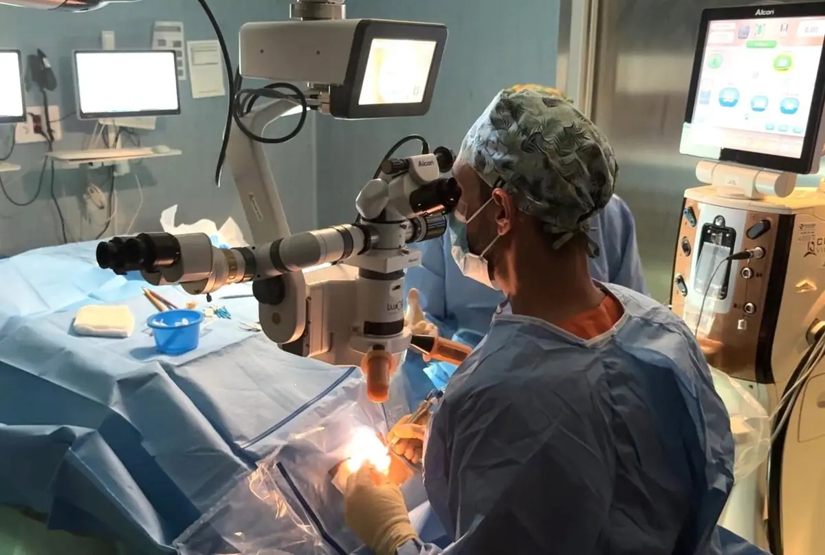 Intervención con microscopio en quirófano Persona con ropa quirúrgica trabaja junto a un microscopio durante una intervención.