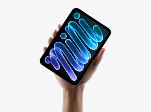 iPad mini 8 sostenido en una mano Una mano sostiene una tableta negra con una pantalla de fondo azul y morado.