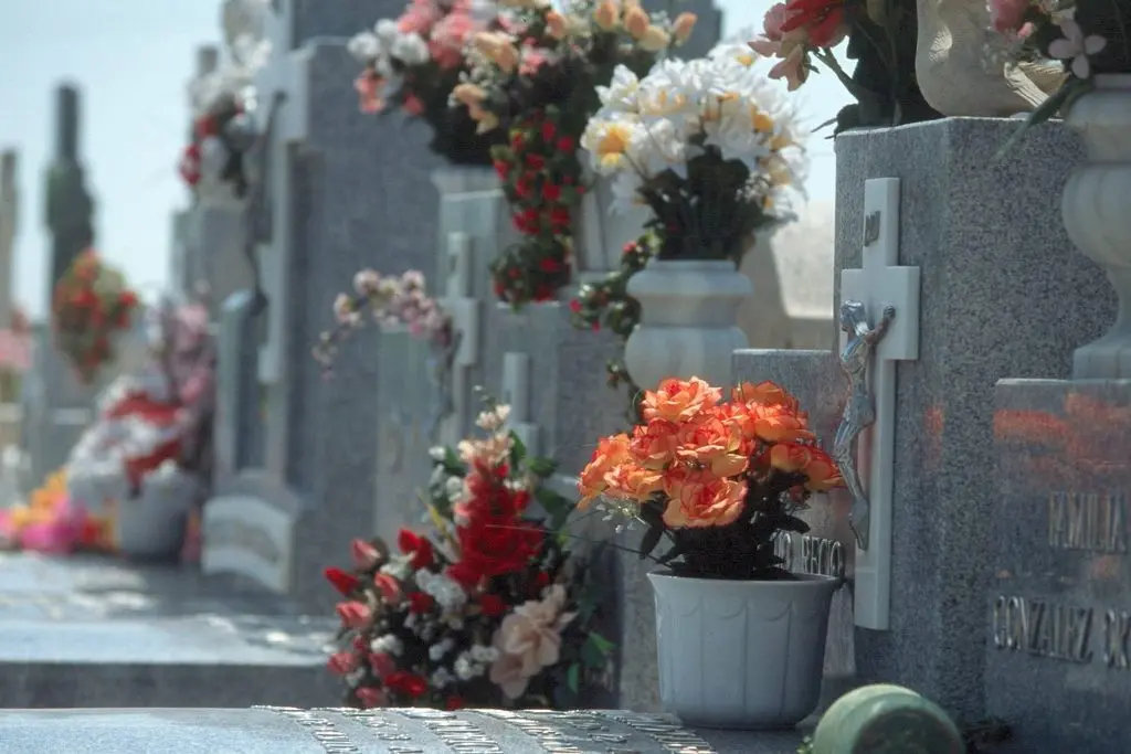 Flores de colores adornan varias lápidas de piedra en un cementerio.