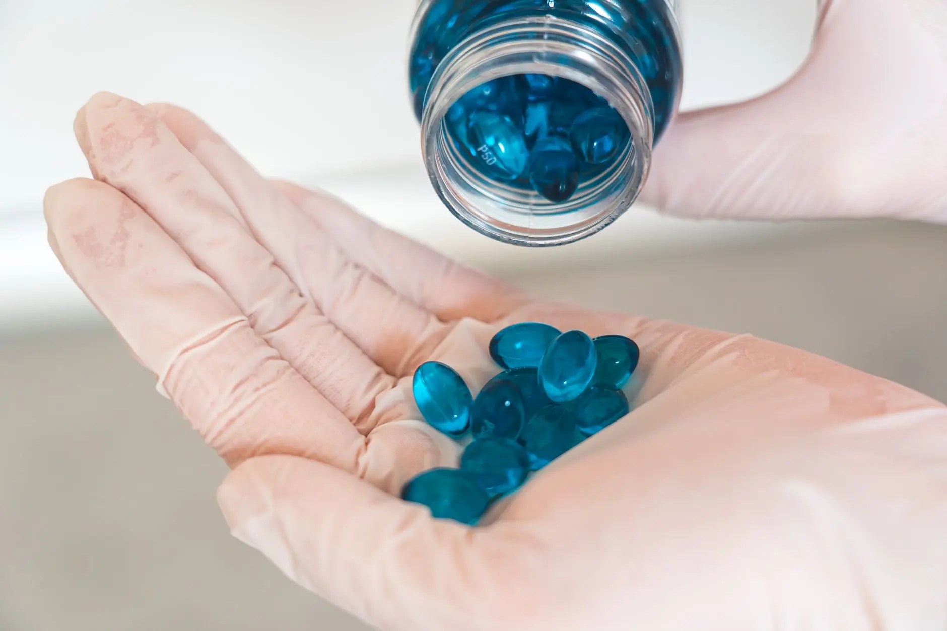 Imagen en primer plano de un trabajador de la salud con guantes de látex vertiendo cápsulas azules de un frasco.