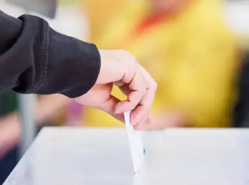 Mano deposita una papeleta en una urna Una mano introduce una papeleta en una urna transparente durante una votación.
