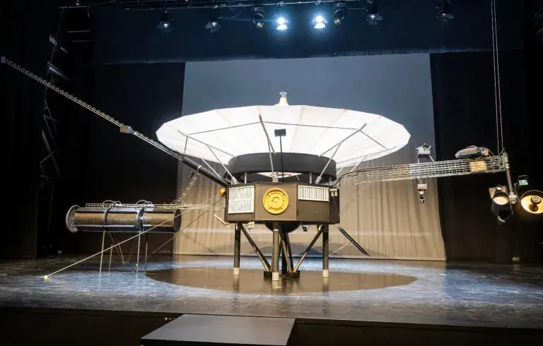 Maqueta de la Voyager 1 en exposición Maqueta de la sonda Voyager 1 expuesta sobre un escenario bajo focos