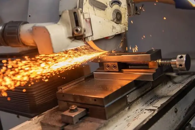Máquina industrial trabaja una pieza metálica y desprende chispas en un taller