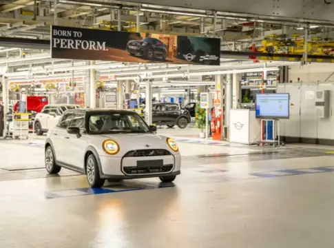 MINI blanco en una nave de producción Un MINI blanco aparece en primer plano dentro de una nave de producción con otros vehículos.
