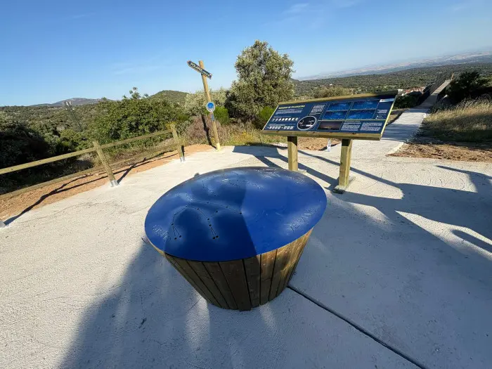 Mirador con mesa circular azul, panel informativo y paisaje de colinas