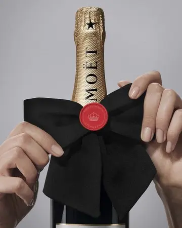 Moët & Chandon transforma sus botellas en regalos de lujo para Navidad con una novedad que se puede personalizar 2 Merca2 Manos ajustan un gran lazo negro alrededor del cuello de una botella Moët