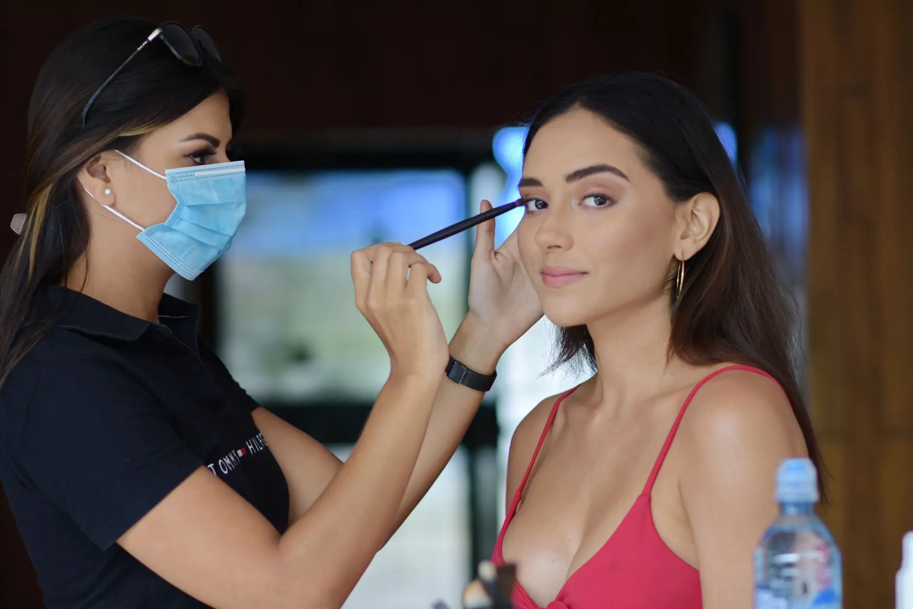 Una maquilladora aplica maquillaje en los ojos a una mujer en interiores, resaltando la belleza y la precisión.