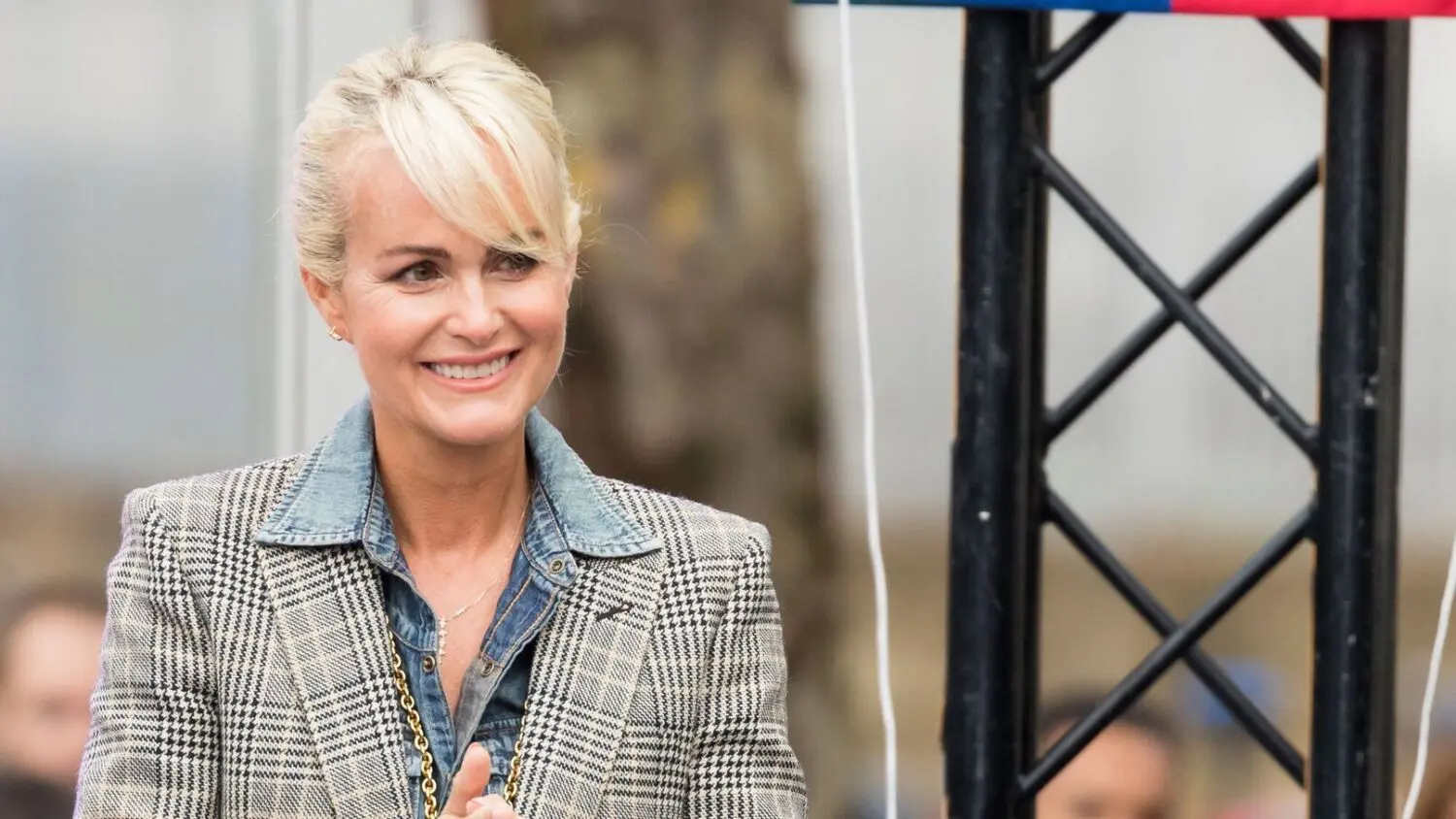 Mujer con blazer de cuadros Mujer sonriente con blazer de cuadros y camisa vaquera junto a una estructura negra
