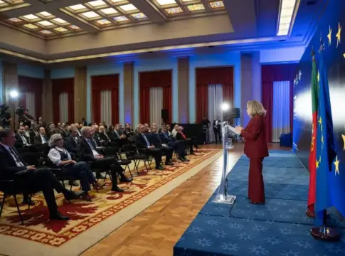 Intervención ante asistentes en un auditorio Una mujer habla desde un atril ante asistentes con banderas de Portugal y la Unión Europea