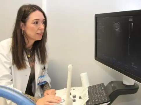 Mujer junto a un equipo de ultrasonido Mujer con bata blanca sentada junto a un equipo de ultrasonido y su monitor