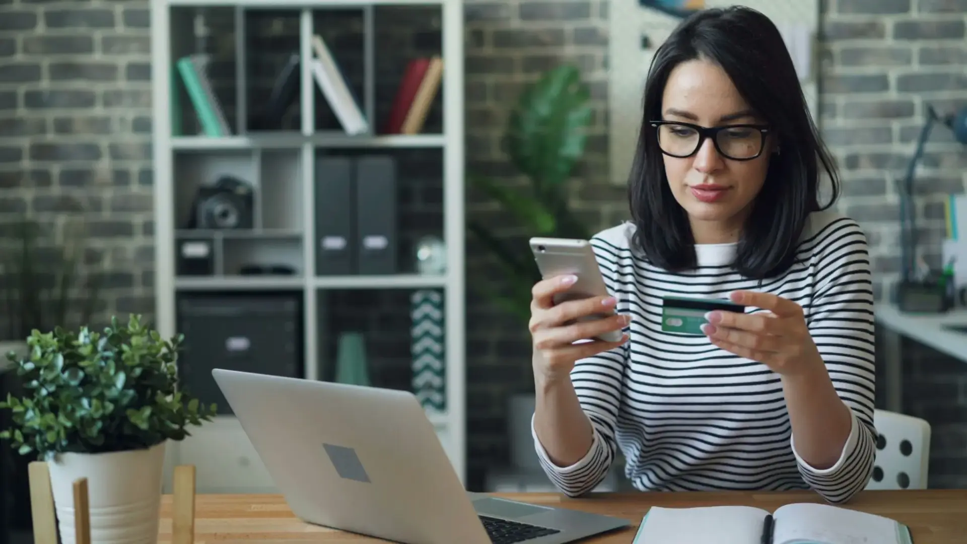 Mujer con móvil y tarjeta junto a un portátil compradores online IA