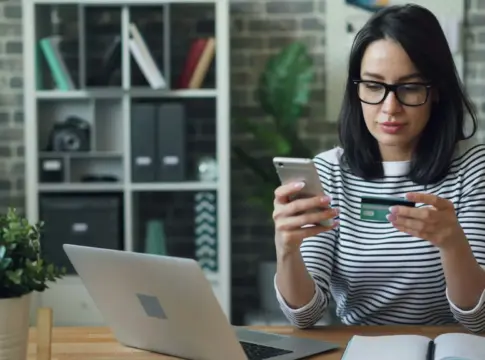 Mujer con móvil y tarjeta junto a un portátil compradores online IA