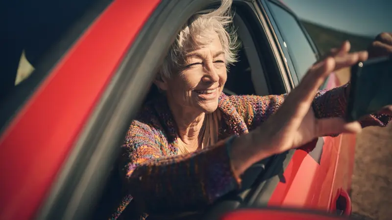 TRIBBU CONFIA A VODAFONE EMPRESAS LA GESTIÓN INTEGRAL DE SU NUBE 1 Merca2 Mujer mayor sonríe y extiende un brazo desde la ventanilla de un coche rojo.