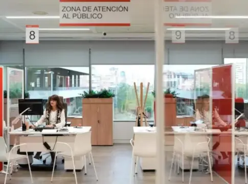 Zona de atención al público Mujer en un escritorio de oficina bajo un letrero de atención al público.
