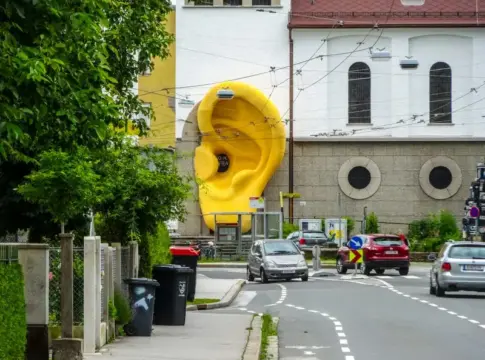 Oreja amarilla junto al tráfico Escultura amarilla con forma de oreja junto a una calle con varios vehículos.