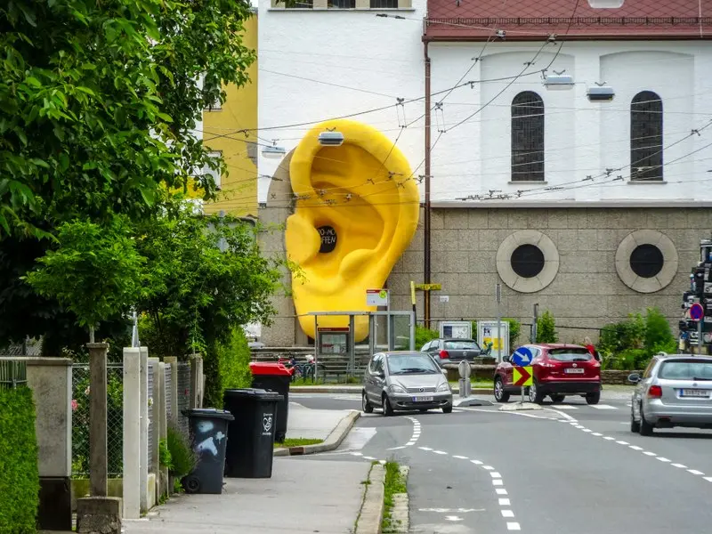 Escultura amarilla con forma de oreja junto a una calle con varios vehículos.