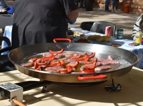 Paellera con ingredientes al aire libre Paellera grande con carne y pimiento rojo sobre un quemador al aire libre