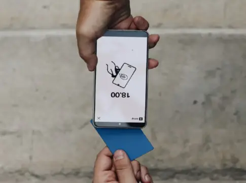 Móvil y tarjeta en una operación de pago Una mano sostiene un móvil con una pantalla de pago y una tarjeta azul.