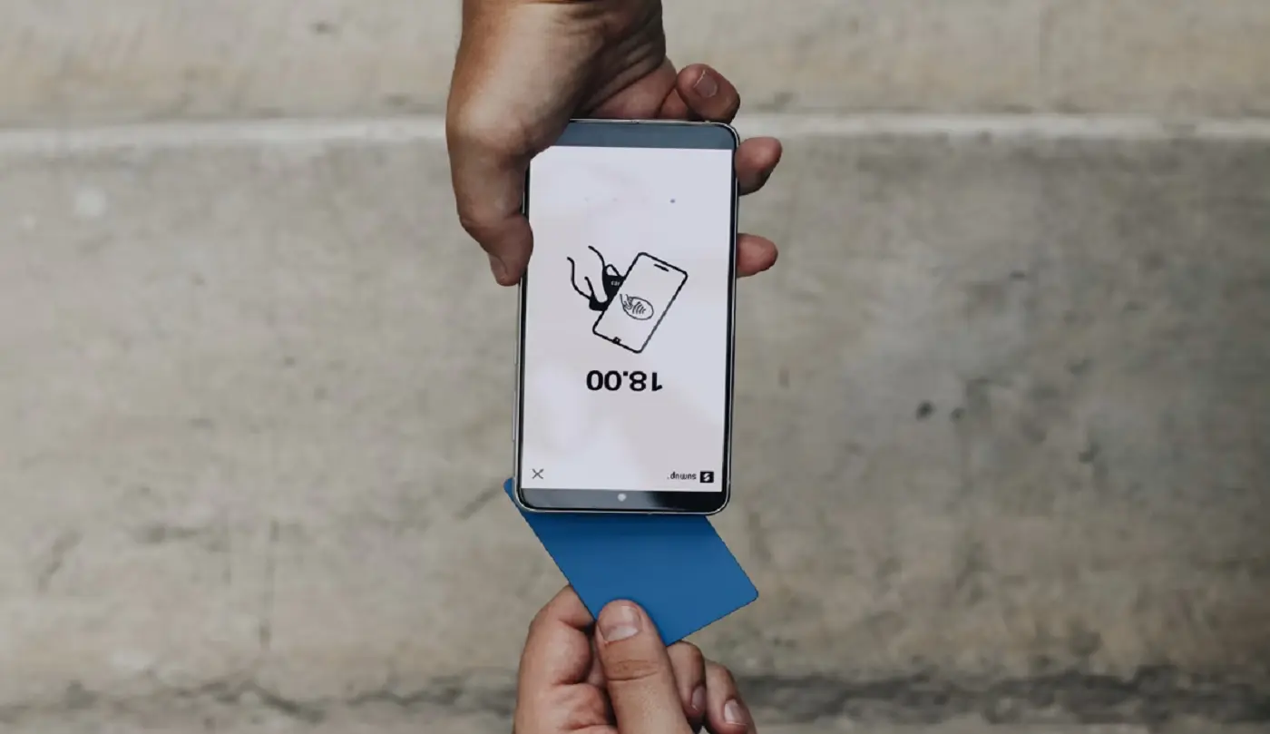 Móvil y tarjeta en una operación de pago Una mano sostiene un móvil con una pantalla de pago y una tarjeta azul.