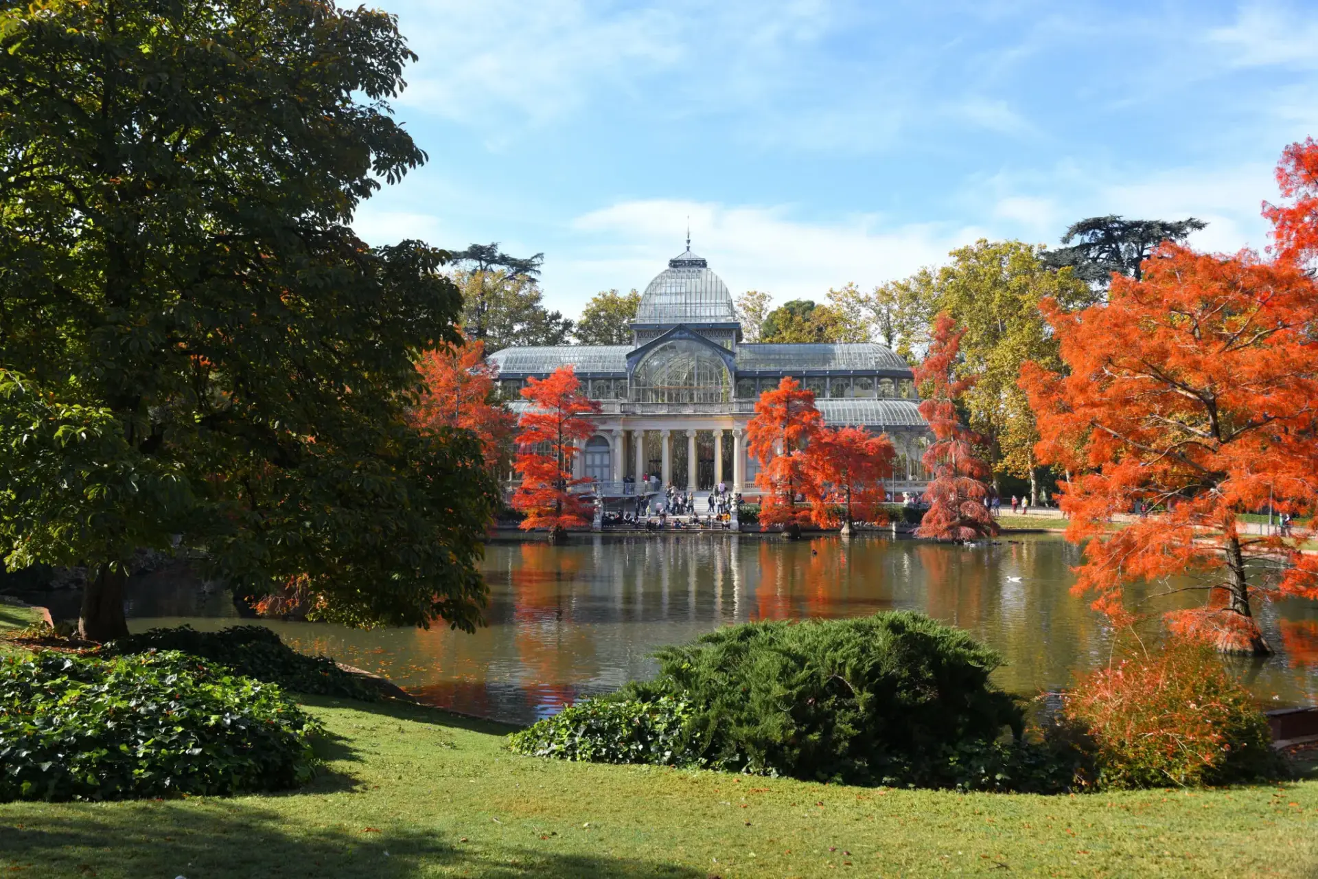 Palacio de Cristal junto al estanque Palacio de Cristal del Retiro junto al estanque, rodeado de árboles otoñales.