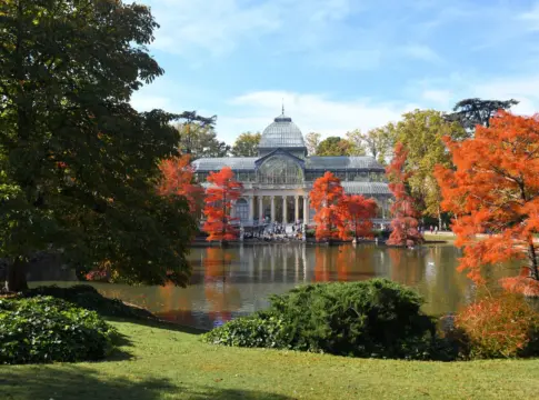 Palacio de Cristal junto al estanque Palacio de Cristal del Retiro junto al estanque, rodeado de árboles otoñales.