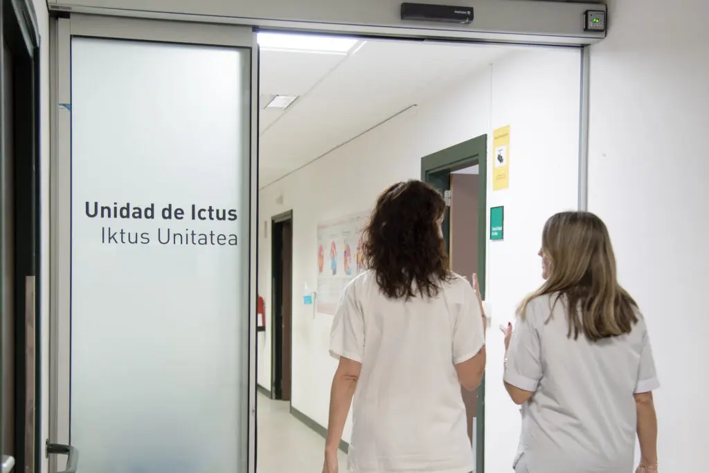 Dos personas con ropa blanca recorren un pasillo junto al rótulo Unidad de Ictus.